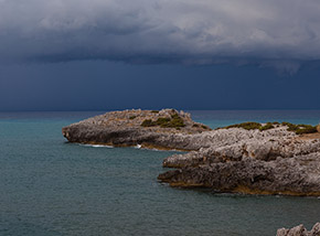 La sottile punta di Capo Grosso si allunga sul mare sotto un cielo carico di pioggia.