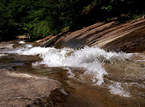 Le onde d’acqua si accavallano e si infrangono in un toboga naturale agli Scivoli del Rio Volpara.