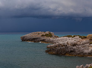 La sottile punta di Capo Grosso si allunga sul mare sotto un cielo carico di pioggia.