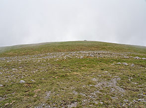 Sulla larghissima e anonima cima de la Mula tra le nubi, in vista dell&rsquo;ometto di vetta.