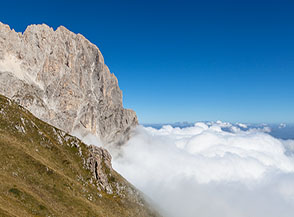 Una soffice e bianca coperta di nubi si alza lentamente da valle al cospetto del Paretone del Corno Grande.