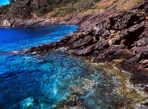 Acque turchesi e cristalline lambiscono le nere rocce vulcaniche a Cala San Paolo.