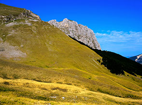 Dai pendii prativi in alta Val di Panico spunta il castello roccioso del Monte Bove Nord.