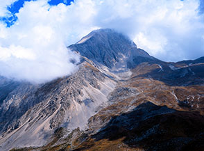 Soffici nuvole s&rsquo;infrangono sul Primo Scrimone e pi&ugrave; in l&agrave; sulla Vetta Occidentale del Corno Grande (sui prati a dx s&rsquo;intravede il Rifugio Garibaldi).